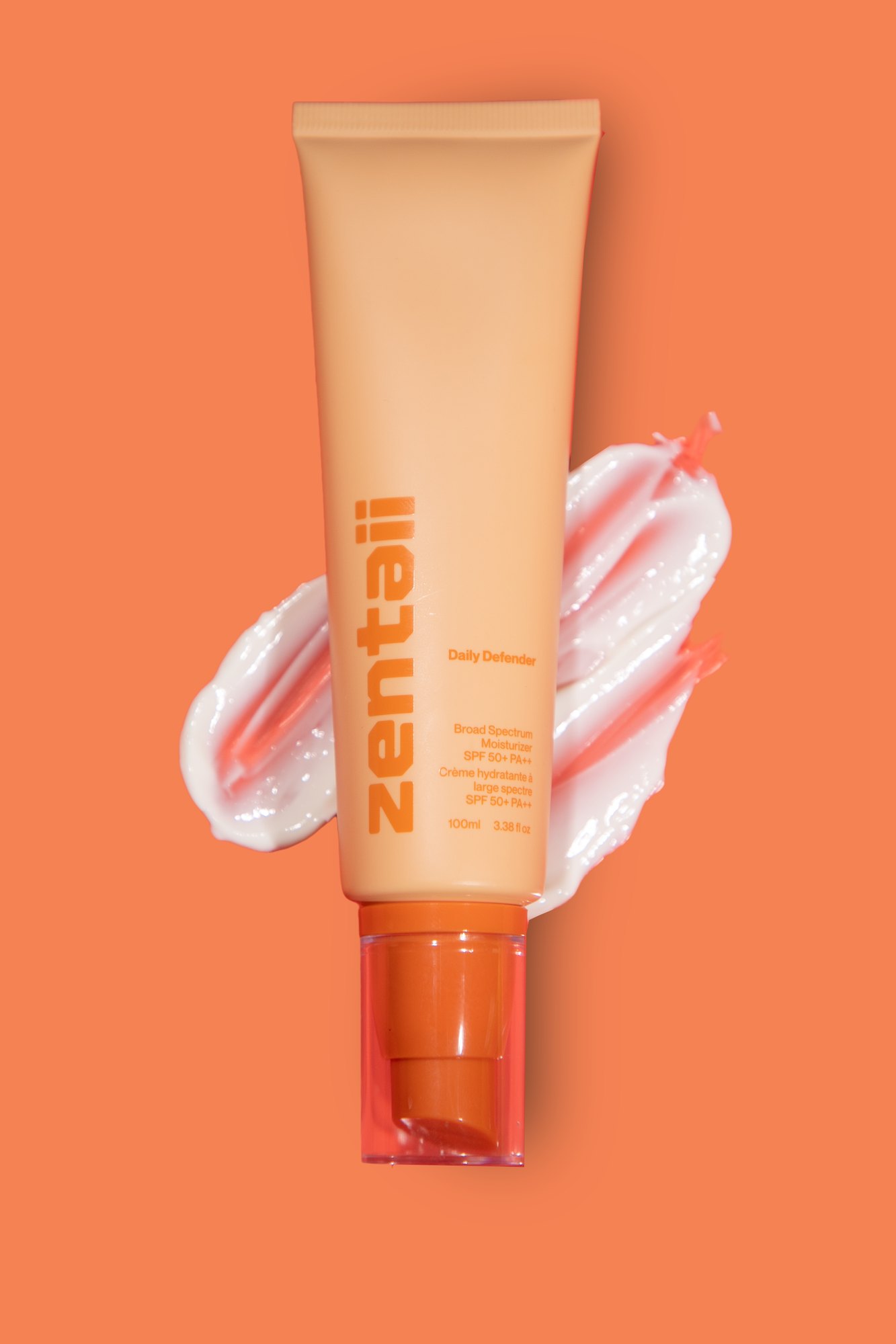 The orange SPF tube on an orange ground with a thick cream swatch swept beside it.